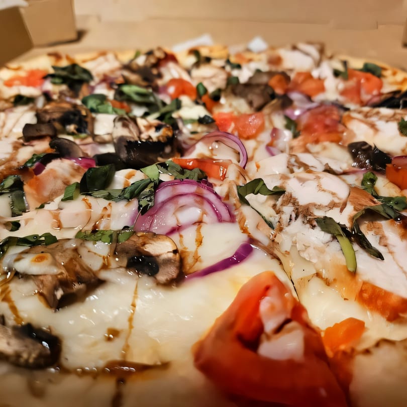 Close-up of a Pizza Spot pizza with mushrooms, red onions, tomatoes, and basil in a box.