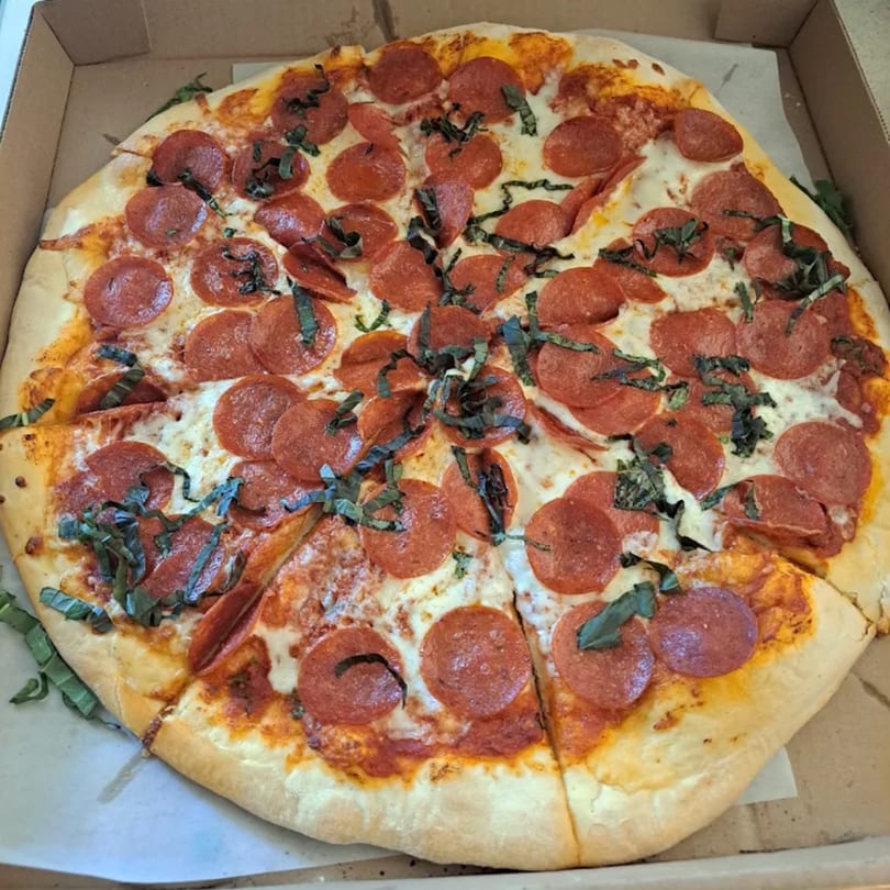 A whole pepperoni and basil pizza from The Pizza Spot in a cardboard box.
