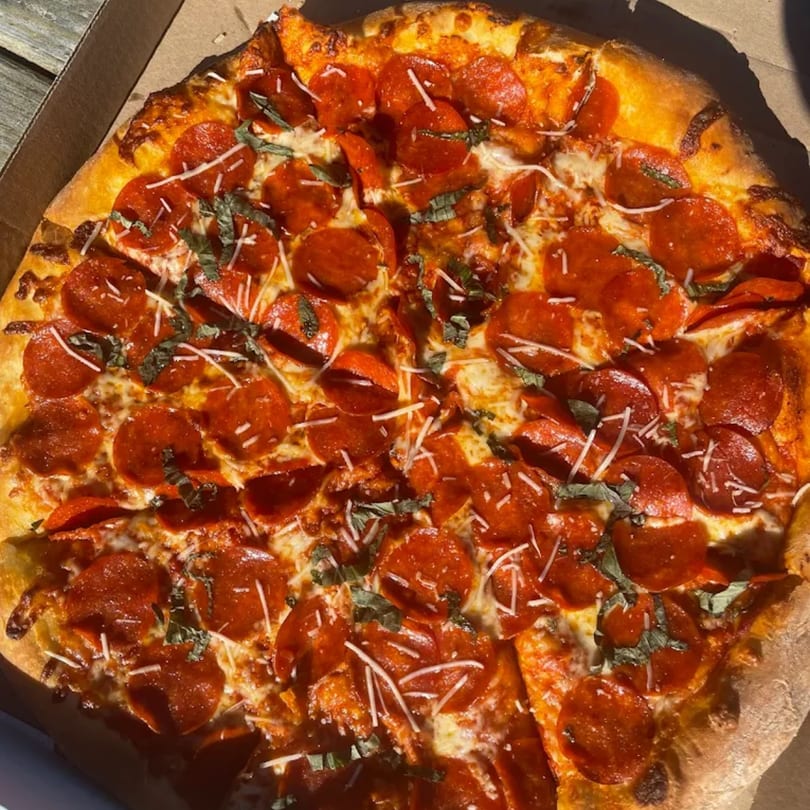 A whole pepperoni pizza from The Pizza Spot, topped with basil and parmesan, in a cardboard box.