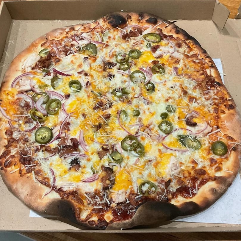 The Pizza Spot's BBQ chicken pizza with red onions, jalapeños, and cheese in a box.