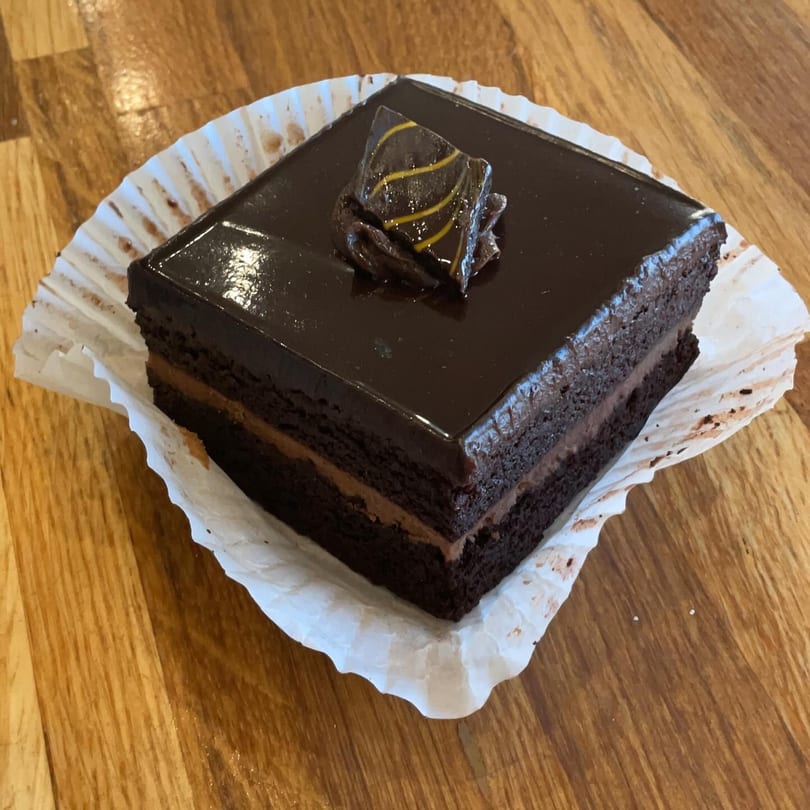 A square slice of chocolate cake with chocolate frosting and a decorative chocolate piece.